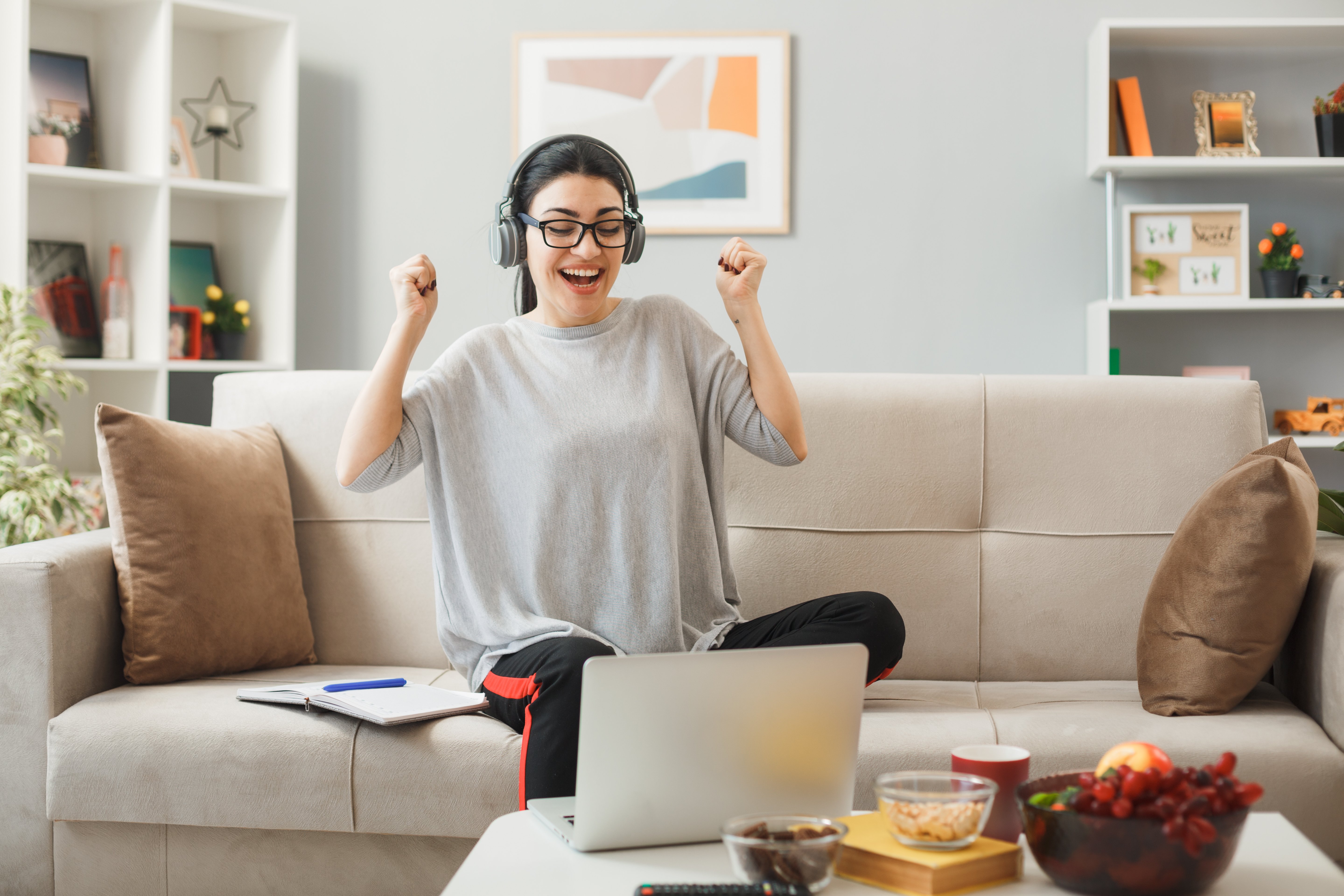 young-woman-wearing-glasses-headphones-sitting-sofa-coffee-table-looking-laptop-living-room